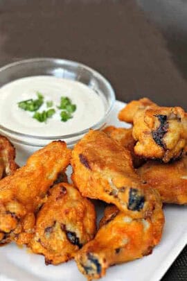 Buffalo chicken wings on a white plate with a side of creamy dipping sauce garnished with chopped herbs.