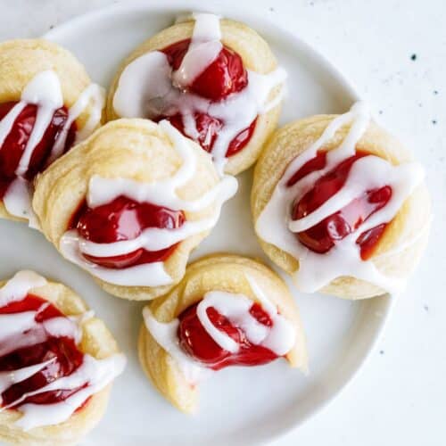 A plate of six cherry Danish pastry cookies drizzled with white icing.