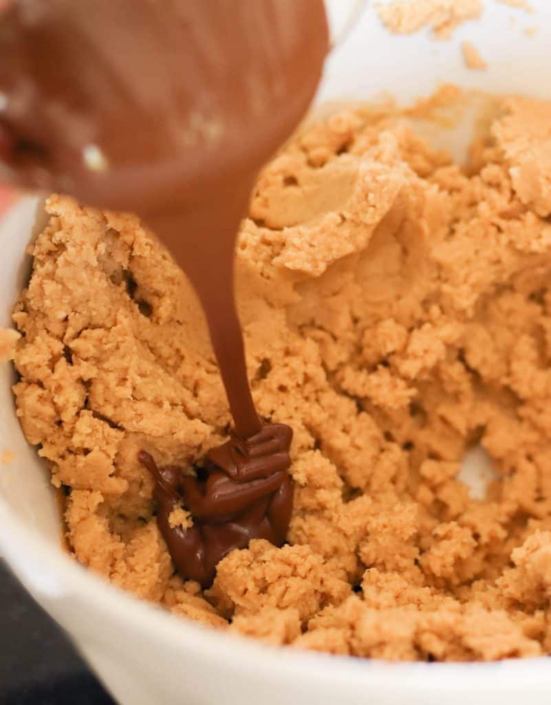 Adding melted Nutella into bowl of peanut butter cookie dough.