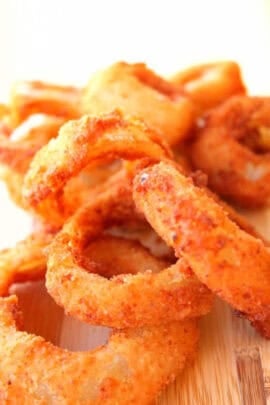 Close-up of a stack of crispy, golden-brown onion rings on a wooden surface.