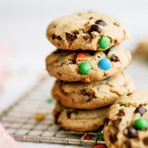 M&M Cookies stacked on a cooling rack with some mini m&m's on the counter.