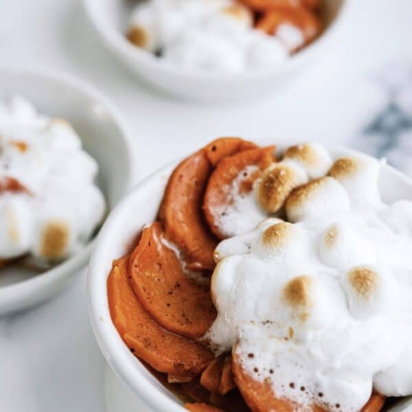 Three bowls of sweet potato casserole topped with toasted marshmallows and white sauce.