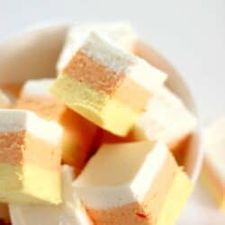 A bowl filled with layered candy corn marshmallows, featuring distinct stripes of white, orange, and yellow.