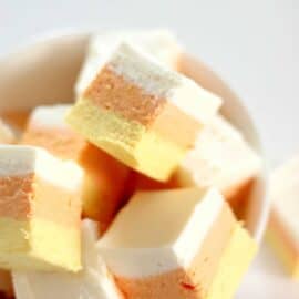 A bowl filled with layered candy corn marshmallows, featuring distinct stripes of white, orange, and yellow.