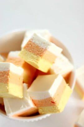 A bowl filled with layered candy corn marshmallows, featuring distinct stripes of white, orange, and yellow.