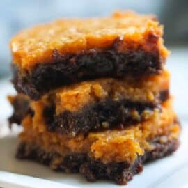 A three-layered brownie with a caramelized top and fudgy interior is stacked on a white plate.