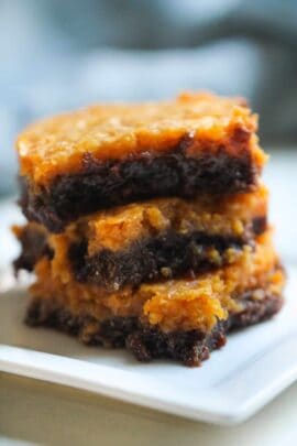 A three-layered brownie with a caramelized top and fudgy interior is stacked on a white plate.