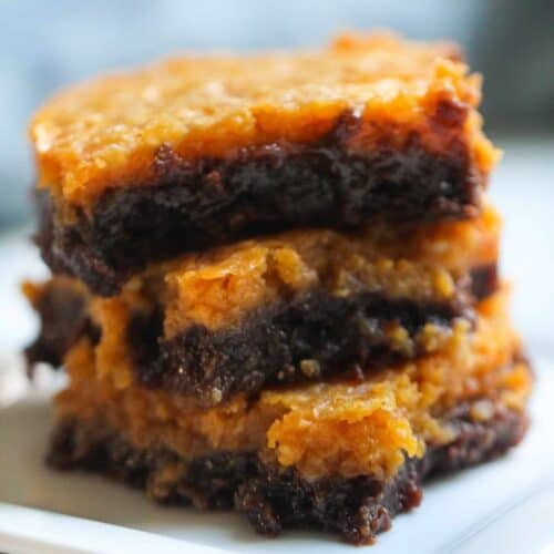 A three-layered brownie with a caramelized top and fudgy interior is stacked on a white plate.