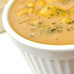 A close-up of a white bowl filled with creamy, pumpkin soup garnished with herbs.