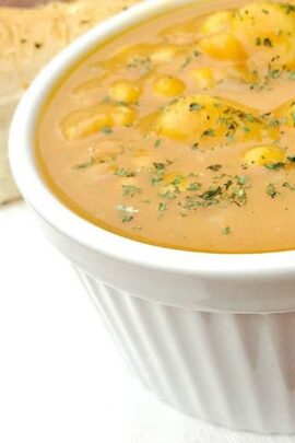 A close-up of a white bowl filled with creamy, pumpkin soup garnished with herbs.