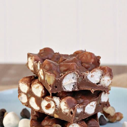 A stack of rocky road chocolate squares with visible marshmallows and nuts, placed on a light blue plate.