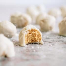 Close-up of white chocolate-covered peanut butter balls, one of which is bitten into, revealing the peanut butter filling.