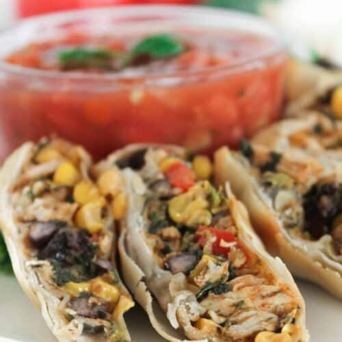 Close-up of sliced stuffed rolls filled with corn, beans, and vegetables on a plate. A bowl of chunky tomato salsa in the background.