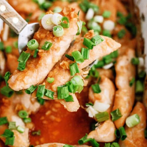 Baked Honey Chicken Tenders in a pan with a spatula lifting 2 tenders out of the baking dish.