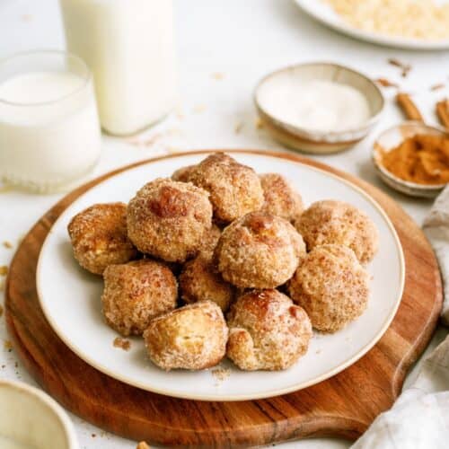 Cinnamon breakfast bites stacked on a plate with a cutting board underneath. A glass of milk and a bottle of milk on the side.