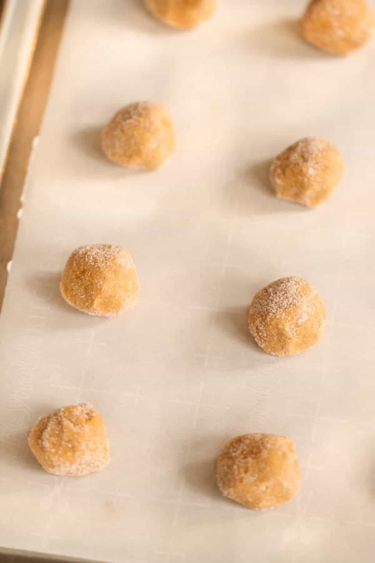 Unbaked cookie dough balls are arranged on a parchment-lined baking sheet.