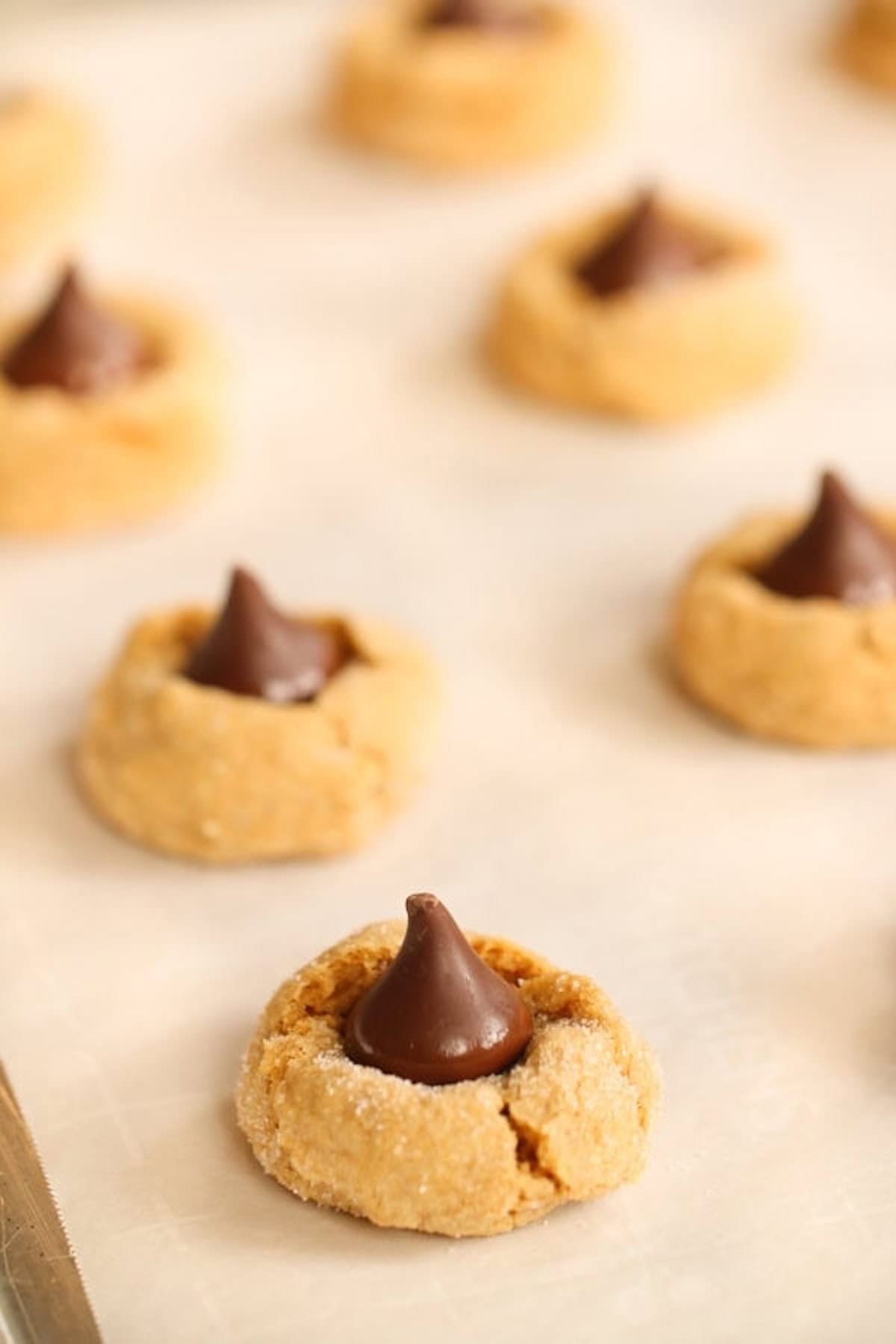 Pumpkin cookies with chocolate kisses on top, placed on a parchment-lined baking sheet.