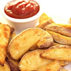 Potato wedges seasoned with spices and served on a plate with a cup of ketchup.