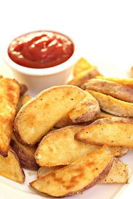 Potato wedges seasoned with spices and served on a plate with a cup of ketchup.