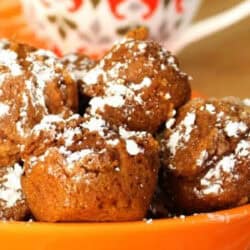 A plate of powdered sugar-dusted chocolate muffins in an orange dish with a patterned mug in the background.