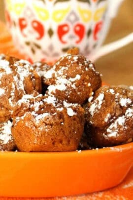 A plate of powdered sugar-dusted chocolate muffins in an orange dish with a patterned mug in the background.