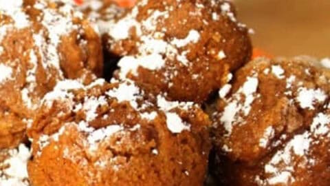 A plate of powdered sugar-dusted chocolate muffins in an orange dish with a patterned mug in the background.