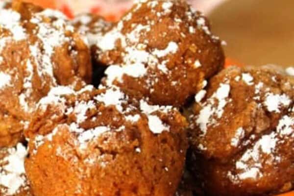 A plate of powdered sugar-dusted chocolate muffins in an orange dish with a patterned mug in the background.