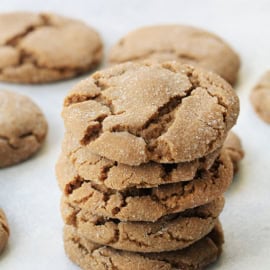 A stack of cracked, round cookies arranged on a white surface with other cookies scattered around.