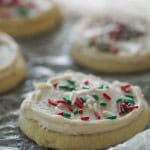 Sugar cookies with white frosting and red, green, and white sprinkles on a textured surface.