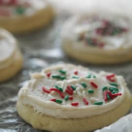 Sugar cookies with white frosting and red, green, and white sprinkles on a textured surface.