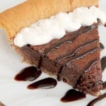 A slice of Chocolate Chess pie on a white plate with chocolate drizzle and whip cream on top.