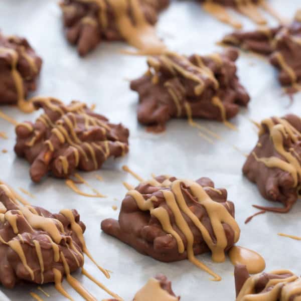 A baking sheet with clusters of chocolate-covered pretzels, drizzled with peanut butter, is arranged in rows.