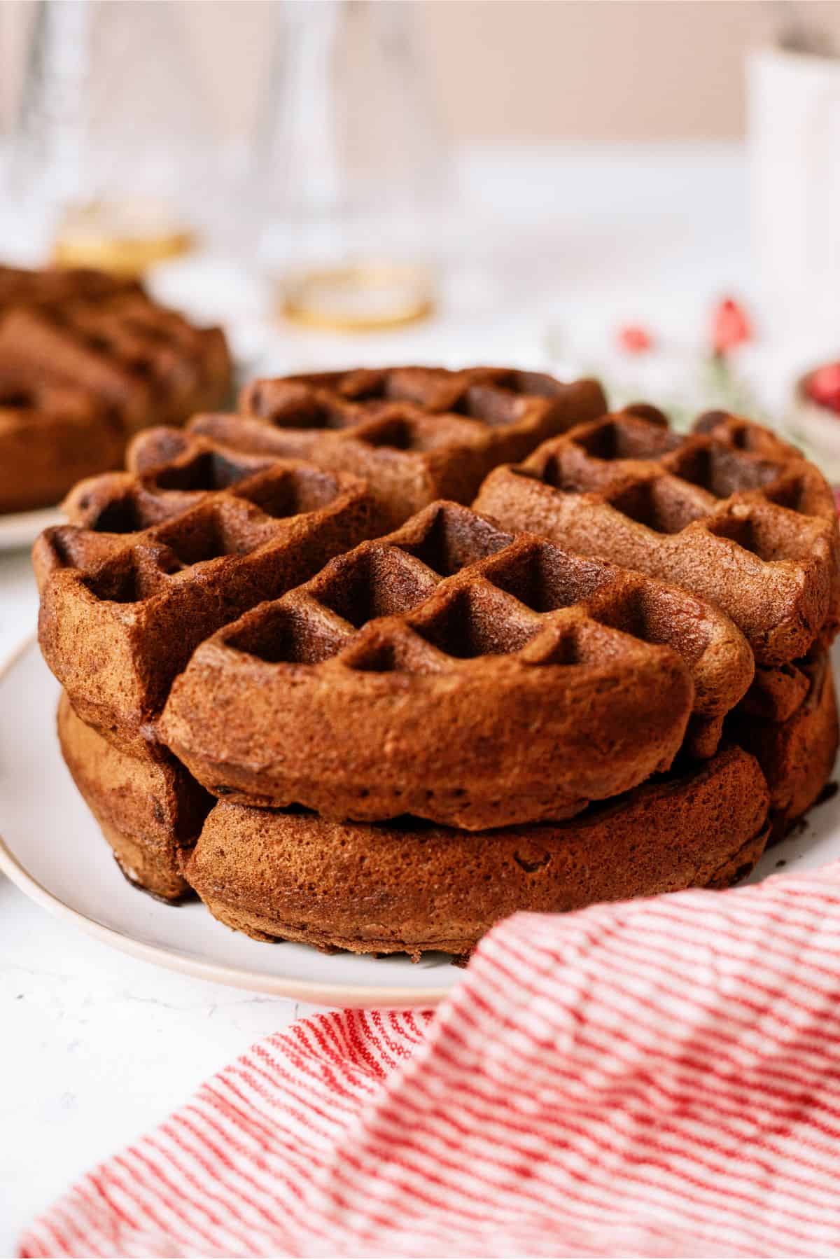 A stack of gingerbread waffles on a white plate, with a red and white striped cloth nearby.