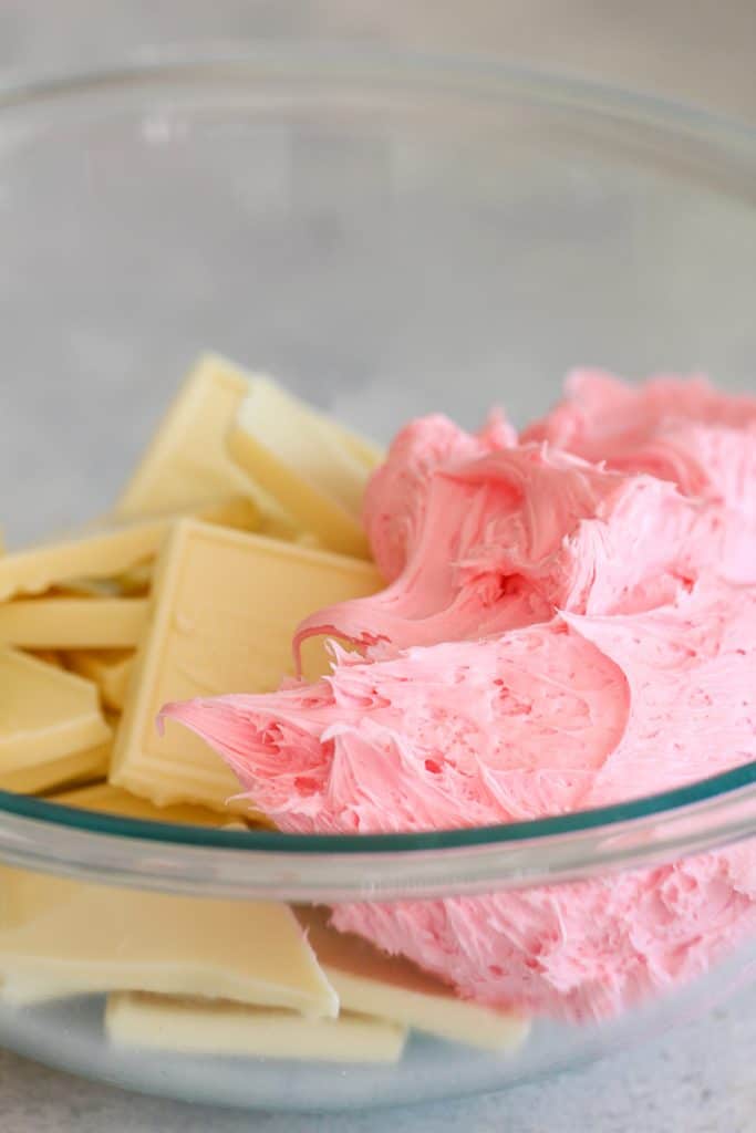 A glass bowl with strawberry frosting and pieces of white chocolate almond bark.