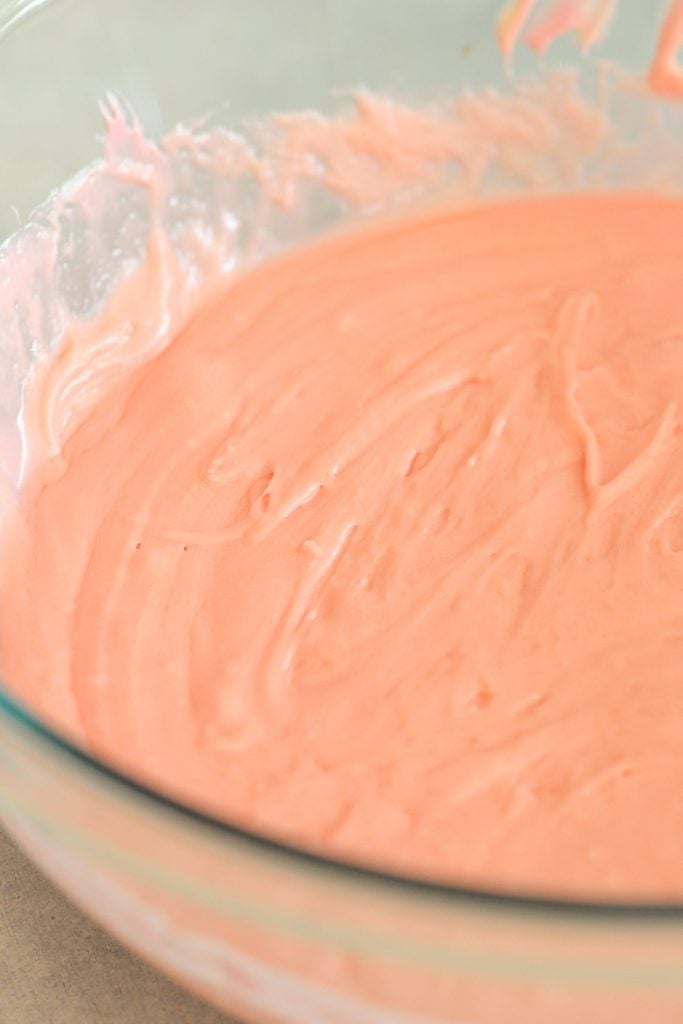 Melted strawberry frosting and almond bark mixed together in a glass mixing bowl.