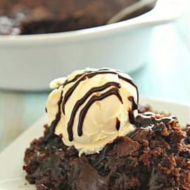 A close-up of a chocolate dessert served on a white plate, topped with a scoop of vanilla ice cream drizzled with chocolate sauce.