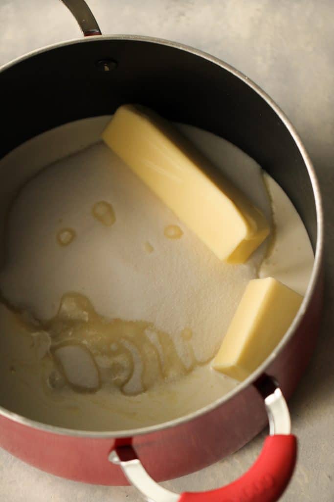 A large pot on the stove top with sugar and sticks of butter in it.