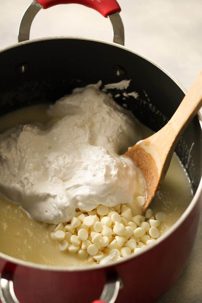 Large pot on the stove top with a wooden spoon stirring in white chocolate chips and marshmallow creme.