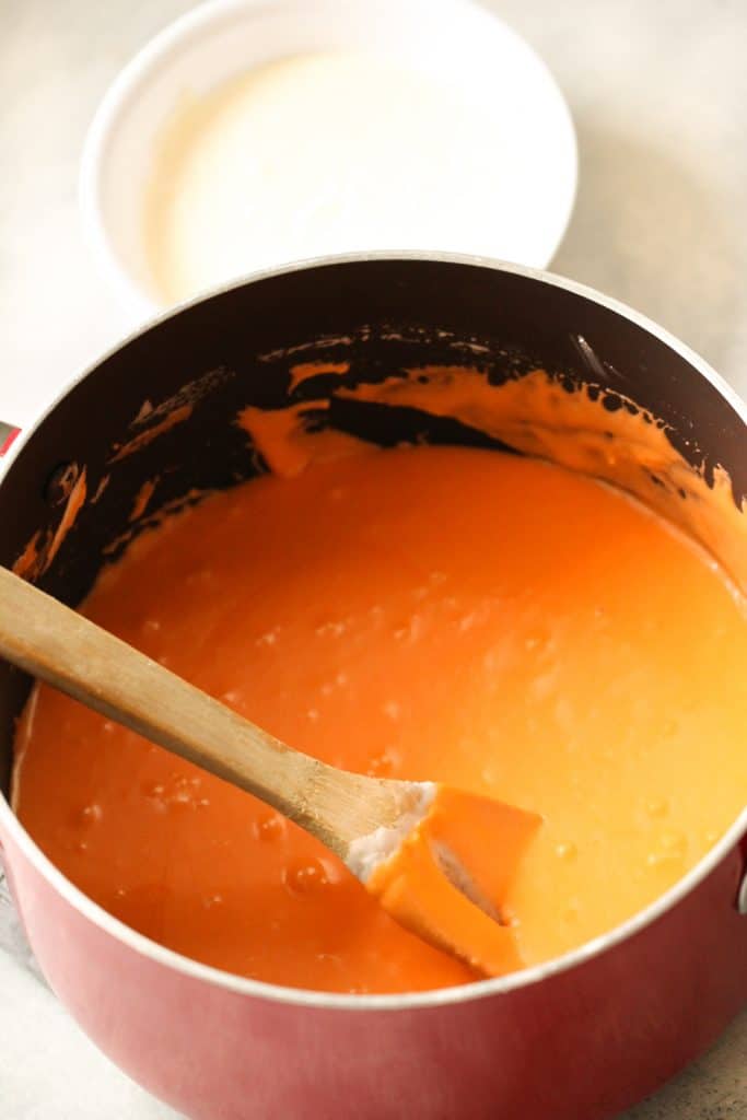 Large pot with a wooden spoon mixing orange fudge batter.