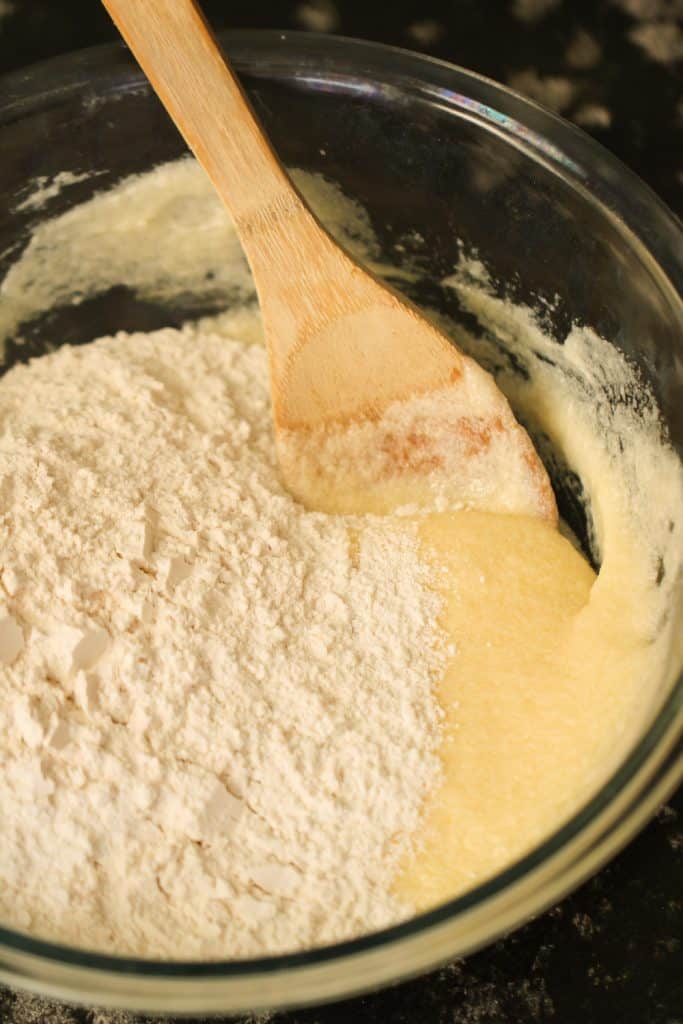 Mixing dry ingredients into wet ingredients in a glass bowl with a wooden spoon.