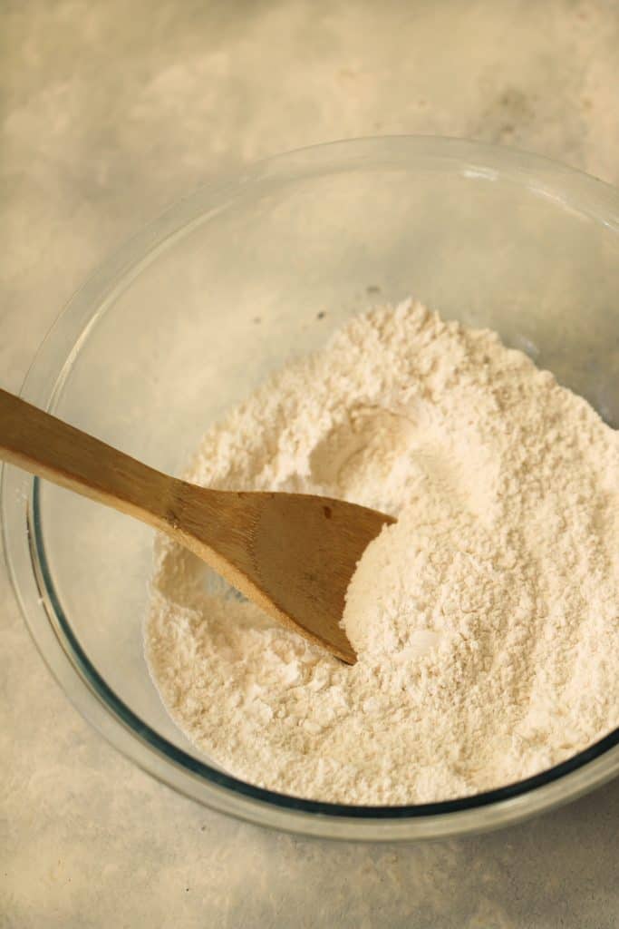 Dry ingredients for Snickerdoodle Cookies mixed together in a glass bowl with a wooden spoon.