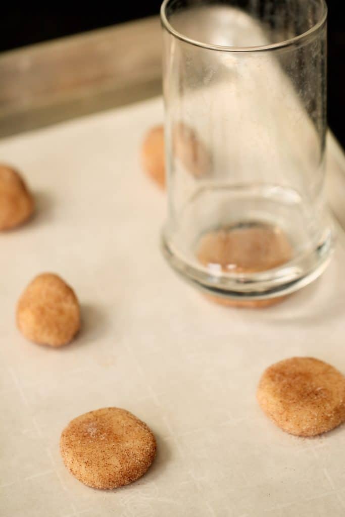 Bottom of glass smashing down the dough balls on a baking sheet lined with parchment paper.