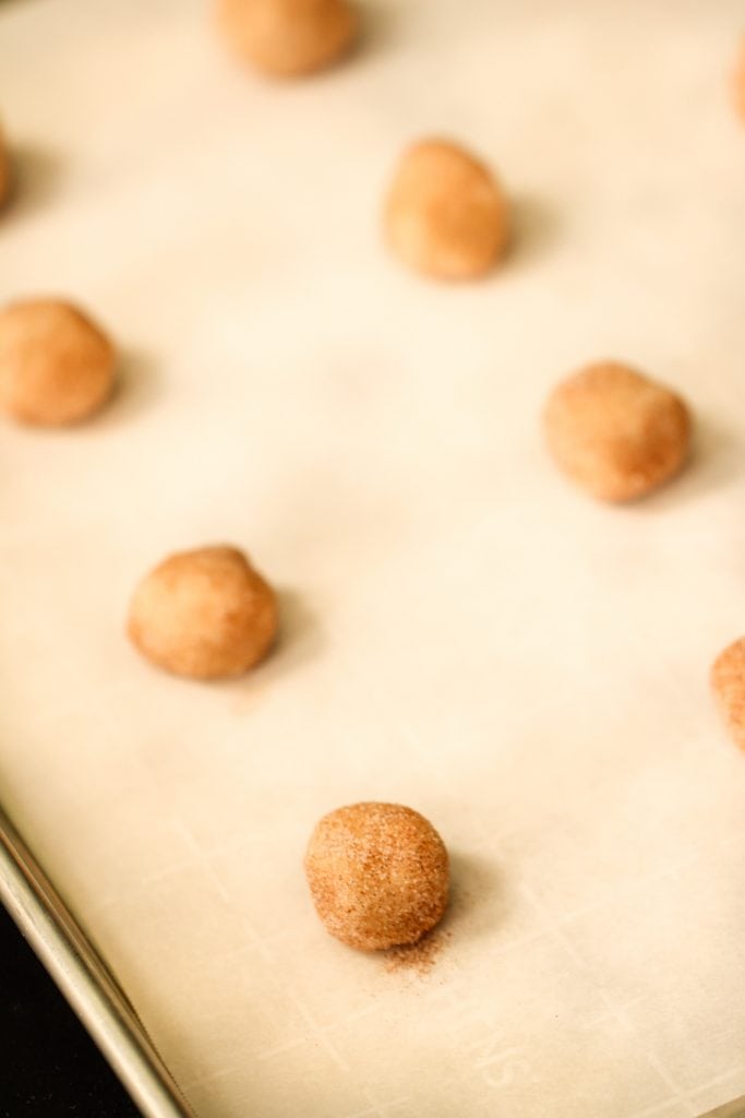 Snickerdoodle Cookie dough rolled into. balls on a parchment lined baking sheet.