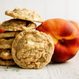 A stack of cookies is placed next to a whole peach on a white surface.