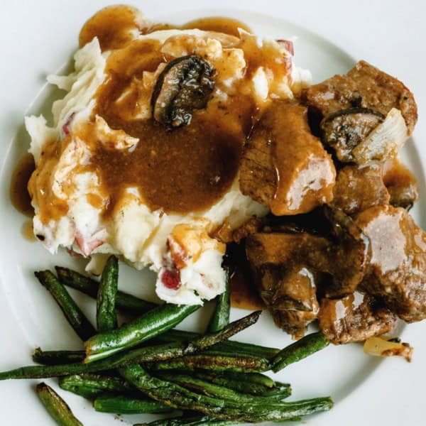 Plate with mashed potatoes topped with gravy, sirloin tips, and green beans on the side.