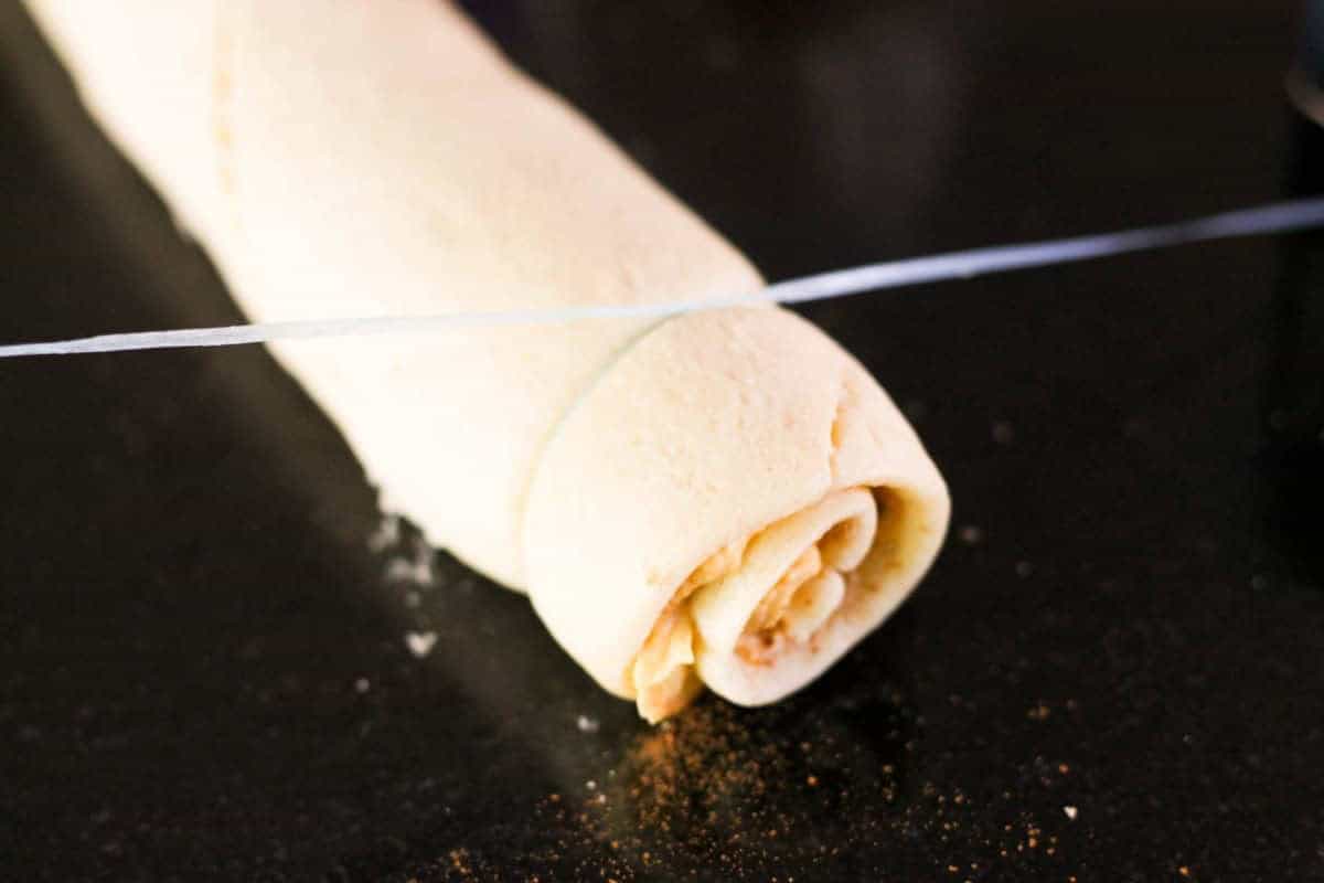 A rolled dough on a dark surface being cut with a piece of string.