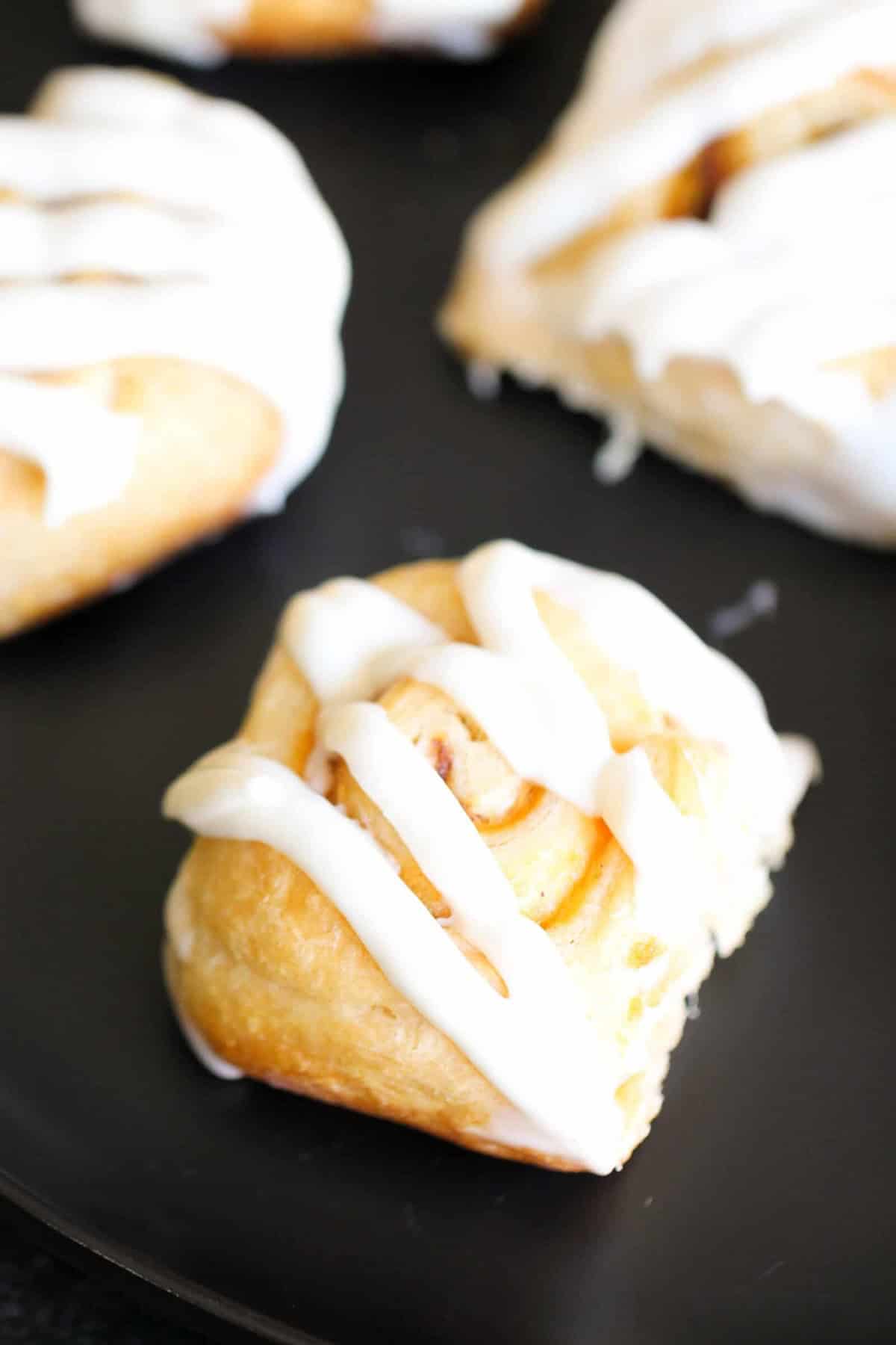 Close-up of pastry rolls with icing, displayed on a black surface.