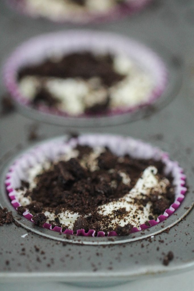 Crumbled oreos on top of cupcake liners filled with oreo and cream cheese mixture.