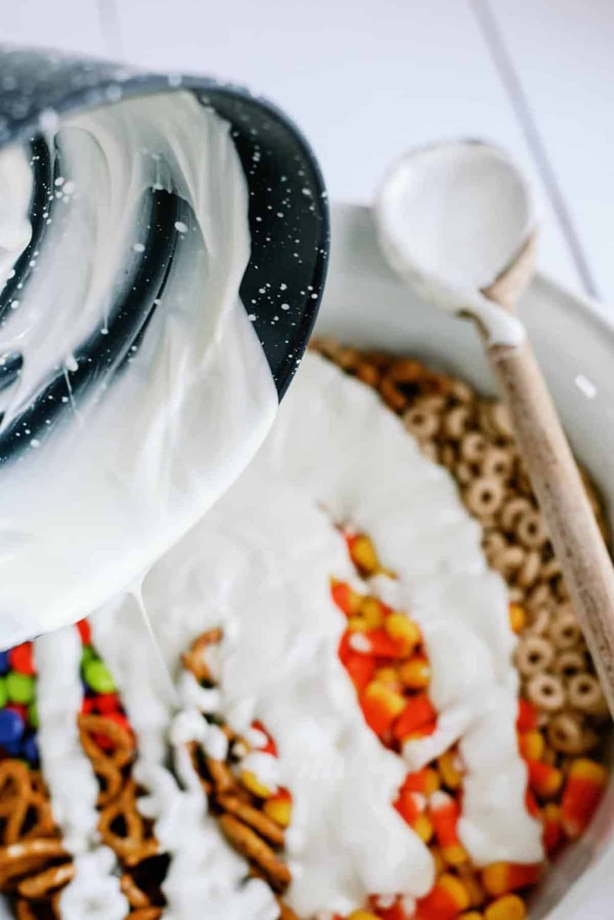 Melted white chocolate being poured on chex mix ingredients