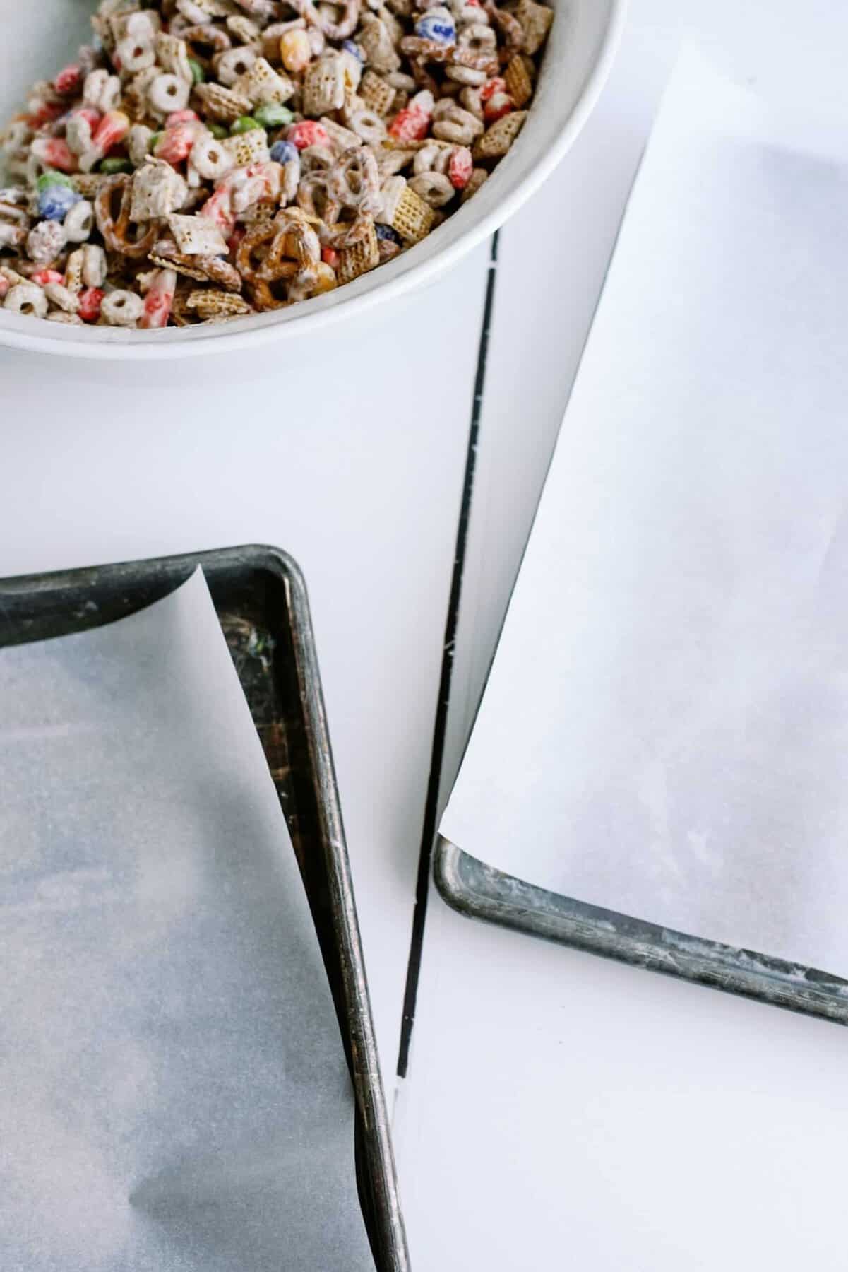 Sheet pans with wax paper next to a bowl of chex mix